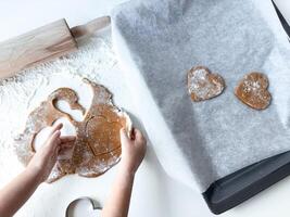 Child baking heart shaped cookies on a floured surface photo