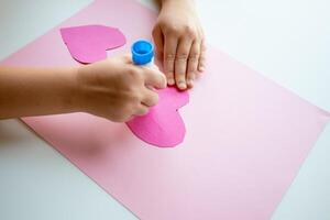 Child making heart shaped craft with pink paper and glue stick photo