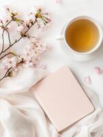 Minimalistic flat lay with cherry blossoms, tea, and notebook on clean white background photo