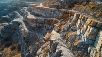 A breathtaking view of a rocky quarry features steep cliffs and winding roads. The landscape is marked by rugged terrain and natural rock formations under clear blue skies. photo