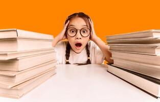 Too Much Homework. Shocked Overworked Asian Schoolgirl Cupping Head In Hands Sitting Between Two Books Stacks Over Yellow Studio Background. photo