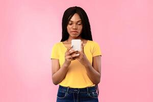 Serious Black Woman Using Cellphone Texting And Browsing Internet Standing In Studio Over Blue Background. Social Media, Gadgets And People. Mobile Application For Smartphone Concept photo