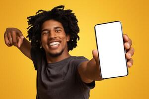 Cool App. Cheerful Black Man Demonstrating Smartphone With Blank White Screen At Camera, Happy African American Guy Showing Copy Space For Mobile Advertisement, Standing On Beige Background, Mockup photo