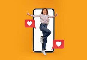 A person enthusiastically poses with thumbs up in front of a large smartphone. The setting is bright and colorful, highlighting themes of love and social media interaction. photo