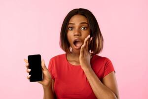 Shocked African American Woman Showing Phone Empty Screen Advertising Mobile Application Posing Over Yellow Studio Background. Wow App, Shocking Message Concept. Mockup photo