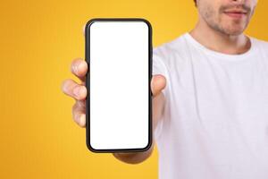 Trendy Mobile Phone. Closeup of bearded male holding smartphone with white empty screen in hand, showing device close to camera. Gadget with blank space, mock up, selective focus, blurred background photo