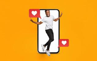 A young man is playfully engaging with a smartphone, showcasing love and connection through social media messages. The background is bright orange, creating a vibrant atmosphere. photo