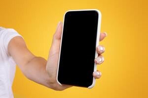 Trendy Mobile Phone. Closeup of female holding smartphone with black empty screen in hand, showing device close to camera. Gadget with blank space, mock up, selective focus, orange blurred background photo