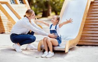 Playground Fun Concept. Joyful Little Girl Riding The Slide Playing With Mom In City Park. Outdoor Weekend Leisure photo
