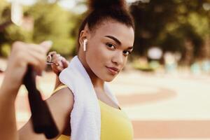 Street Workout. Portrait of confident fit African American woman in earbuds warming up and exercising at park, stretching her arms and chest with equipment, posing looking at camera, free copy space photo