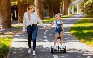 Happy Mom Teaching Little Daughter To Ride Segway Enjoying Day In City Park. Family Fun On Weekend. photo
