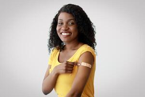 Covid-19 Immunization And Vaccination. Cheerful Black Lady Showing Vaccinated Arm After Antiviral Injection Shot Posing Sitting On Gray Studio Background. Flu Protection. I Got My Vaccine Concept photo