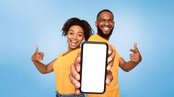 Check this out, cellphone display mockup. Positive African American couple pointing at cellphone with empty screen on blue background, selective focus. Template for mobile app, website or online ad photo