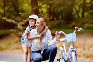 Daughter Hugging Mother Learning To Ride A Bicycle In Park, Wearing Protective Helmet. Family Weekend Adveture Concept photo