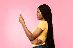 Side View Of Serious Black Female Using Smartphone With Face ID Application For Biometric Verification Standing Over Blue Studio Background. Mobile Technology Concept photo