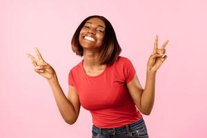 Toothy African American Woman Gesturing V-Sign Victory Symbol To Camera Posing Over Yellow Background. Studio Shot Of Female Showing Peace Gesture With Both Hands Concept photo