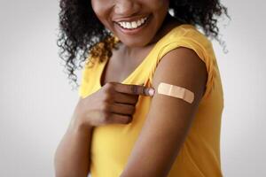 Coronavirus Vaccination. Covid-19 Vaccinated Black Woman Showing Arm After Vaccine Injection Touching Medical Plaster Bandage After Antiviral Injectioin On Gray Studio Background. Virus Protection photo