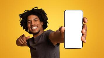 Joyful Black Guy Demonstrating Smartphone With Blank White Screen In His Hand, Cheerful Young African American Man Showing Free Copy Space For Your Ad Or Design, Standing On Beige Background, Mockup photo