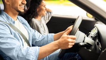 Smiling young middle-eastern man and woman sitting in the luxury car, cheerfully looking at road, having conversation, happy multiracial lovers having weekend trip together, driving auto photo