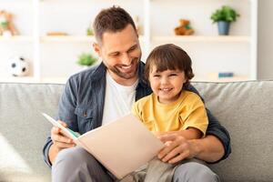 Family and upbringing concept. Close up portrait of happy little boy enjoying storytelling time with his daddy, sitting in armchair with big book photo