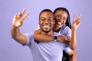 Romantic Black Couple Having Fun Together, Showing V Peace Symbol Sign Gesture With 2 Two Fingers, Cheerful African American Guy Piggybacking Happy Girlfriend, Joyful Woman Riding On Guy's Back photo