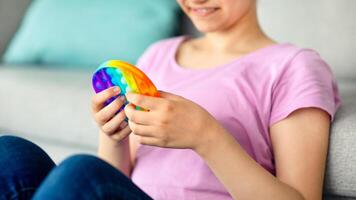 Cropped view of Indian teenage girl playing with antistress POP IT toy at home, closeup of hands. Unrecognizable adolescent enjoying antistress sensory fidget plaything, relaxing indoors photo