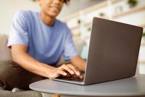 Web based schooling. Cropped view of black teen guy using laptop, speaking to friends on webcam, making home assignment indoors. Unrecognizable adolescent using portable pc, closeup photo