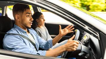 Shocked middle-eastern young couple having car accident or got stuck in traffic while travelling, sitting inside automobile, looking at road, gesturing and resenting, shot from auto dashboard photo