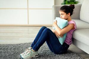 Teen depression during coronavirus lockdown. Stressed Indian teenage girl sitting on floor at home, hugging pillow, suffering from lack of communication, feeling lonely at times of covid quarantine photo