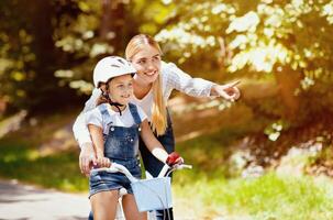 Mom Teaching Daughter To Ride A Bicycle Encouraging Her And Showing Direction Spending Time Together In Park Outside. Family Adveture. photo