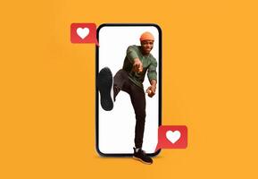 A person playfully poses in front of a bright orange background, emerging from a smartphone. Heart icons indicate active social media engagement, conveying joy and love. photo