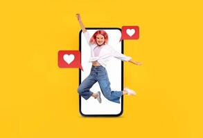 A joyful person jumps in front of a large smartphone displaying heart icons, symbolizing love and communication. The vibrant yellow background enhances the lively atmosphere of modern dating. photo