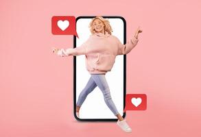 A cheerful individual is stepping out of a smartphone, celebrating love and connection. The bright pink background and floating heart icons emphasize the theme of social media interaction. photo