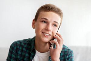 Smiling teenager talking on mobile phone with friends, sitting at home alone, empty space photo