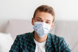 Teenager in protective mask sitting in front of laptop at home, online education during isolation photo