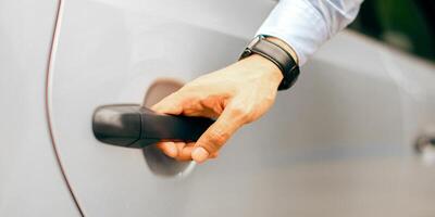 Unrecognizable man hand with expensive watch on opening luxury car back door, closeup photo. Businessman getting inside the auto, cropped of driver assisting manager, open automobile door photo