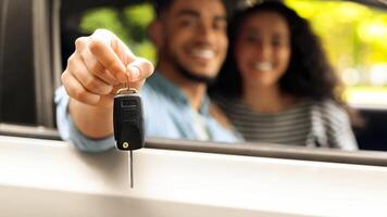 Closeup of automatic key from car in middle-eastern guy driver hand, blurred background. Unrecognizable arabic couple sitting inside nice automobile, showing key from auto, car renting concept photo