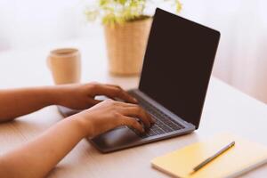 Technology, Communication, Remote Work And Learning. Closeup of unrecognizable african american woman typing on laptop keyboard, sitting at desk with notebook, plant and cup of coffee, selective focus photo