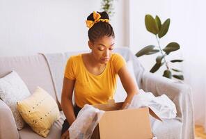 Wrong Package. Portrait of confused and dissatisfied african american woman unpacking box and looking inside, not happy by bad delivery service sitting on sofa at home. Shipping mistake, copy space photo