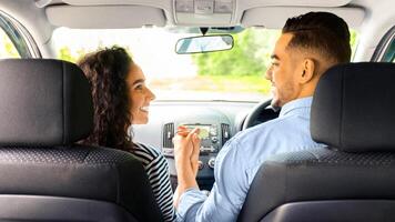 Loving multiracial couple holding hands and smiling to each other while sitting in comfortable auto, back view. happy arab guy having car trip with his beautiful girlfriend, summer vacation concept photo