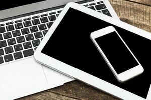 Modern technology setup featuring a laptop, tablet, and smartphone on a wooden surface photo
