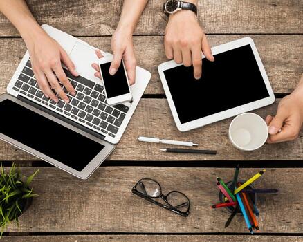 People engaging with various devices while working at a wooden table in a co-working space during daytime photo