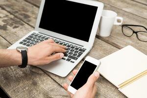Work setup with laptop and smartphone on wooden table in cozy environment during the afternoon photo