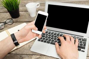 Individual interacting with a laptop and smartphone on a wooden table in a casual workspace setting photo