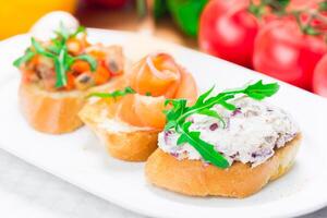 Three colorful tapas served on a white plate in a bright kitchen setting during a casual gathering photo