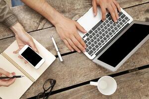 Collaboration at a wooden table with laptop, notebook, and smartphone during a productive work session photo