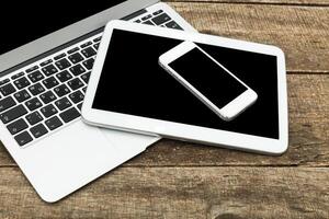 Modern technology setup with laptop, tablet, and smartphone on rustic wooden table for productive work days photo