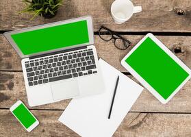 Workspace with multiple devices and stationary on a wooden table during the day photo