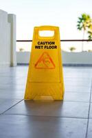 Caution sign indicating wet floor near pool area on a sunny day with palm trees in background photo