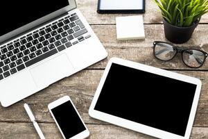 Organized workspace with laptop, tablet, mobile phone, and greenery on a rustic wooden table during a sunny day photo